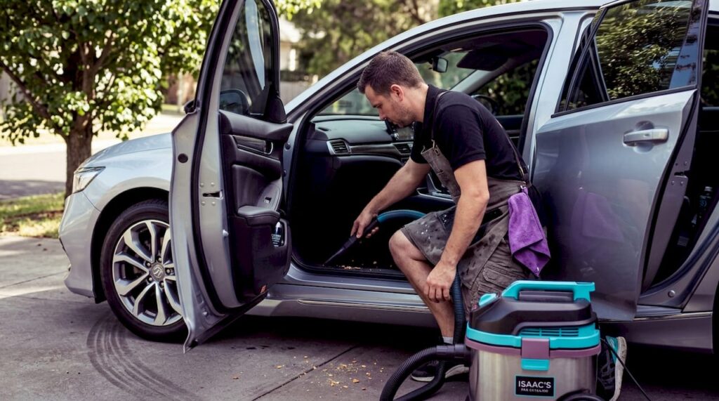 Auto detailer vacuuming car interior in driveway